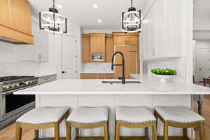 Kitchen featuring a kitchen breakfast bar, suspended lighting, built in appliances, a peninsula, and light stone countertops