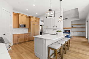 Two tone kitchen with dual tone cabinets, light stone counters, a warm lit fireplace, hanging lights, and light wood finished floors