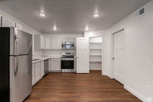 Kitchen with stainless steel appliances, light countertops, dark wood finished floors, and white cabinetry