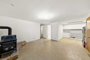 Unfurnished living room featuring light flooring, a wood stove, concrete block wall, and electric water heater