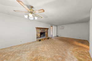 Unfurnished living room featuring a stone fireplace, ceiling fan, and concrete block wall
