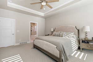 Bedroom with a tray ceiling, carpet flooring, ceiling fan, and ensuite bathroom