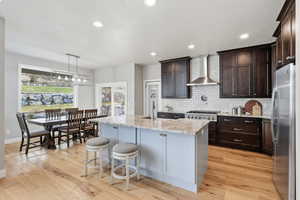 Kitchen featuring light stone counters, stainless steel appliances, decorative backsplash, light wood finished floors, and a center island with sink