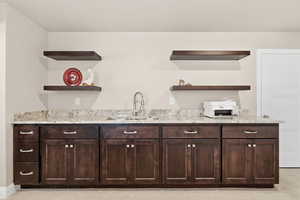 Bar with open shelves, dark wood finish cabinets, and light stone counters