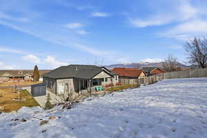 Snow covered rear of property featuring a patio area, stucco siding, a mountain view, and a shingled roof