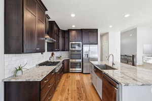 Kitchen with light wood-style flooring, light stone countertops, stainless steel appliances, recessed lighting, and an island with sink