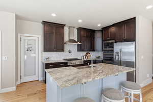 Kitchen with stainless steel appliances, light wood-type flooring, an island with sink, light stone counters, and decorative backsplash