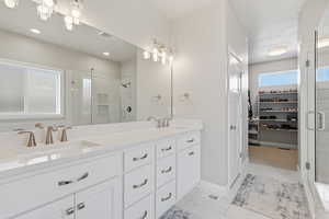 Full bath featuring a shower stall, a walk in closet, double vanity, suspended lighting, and light tile patterned floors