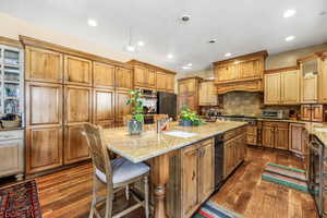 Kitchen with a breakfast bar, light stone countertops, an island with sink, pendant lighting, and wood finish cabinets