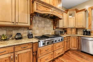 Kitchen with stainless steel appliances, light stone countertops, dark wood finished floors, and backsplash