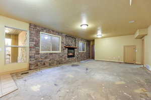 Unfurnished living room featuring a brick fireplace, a textured ceiling, an accent wall, and concrete floors