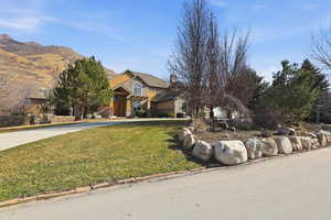 View of front facade featuring stone siding, a front yard, a chimney, and a mountain view