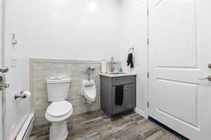 Half bathroom featuring tile walls, vanity, a baseboard radiator, dark wood-style flooring, and wainscoting