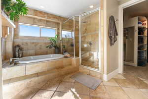 Bathroom featuring stone tile flooring, a garden tub, a stall shower, a walk in closet, and recessed lighting