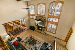 Carpeted living room featuring ceiling fan, a stone fireplace, and a high ceiling
