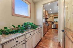 Kitchen featuring dark wood-type flooring, stainless steel dishwasher, light stone countertops, recessed lighting, and cream cabinetry