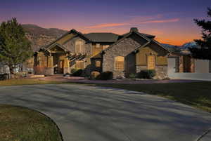 View of front of home with driveway, a yard, a garage, a chimney, and stone siding