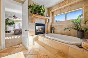 Full bathroom with stone tile floors, a bath, a fireplace, ensuite bath, and healthy amount of natural light