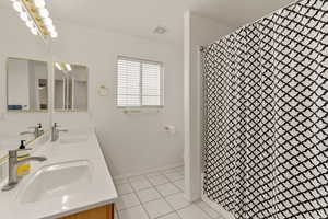 Bathroom featuring double vanity, a shower with curtain, and light tile patterned floors