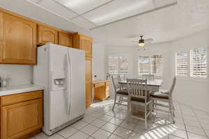 Kitchen with white fridge with ice dispenser, tile countertops, light tile patterned floors, ceiling fan, and a textured ceiling