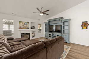 Living area featuring light wood-style floors, a glass covered fireplace, lofted ceiling, and ceiling fan
