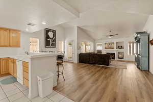 Kitchen featuring a fireplace, light brown cabinetry, a textured ceiling, a breakfast bar area, and open floor plan
