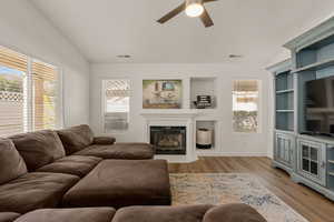 Living room with a glass covered fireplace, light wood-style floors, ceiling fan, and lofted ceiling