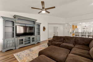 Living room with ceiling fan, light wood-type flooring, and vaulted ceiling