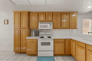 Kitchen featuring tile counters, white appliances, light tile patterned floors, a textured ceiling, and brown cabinetry