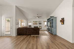 Living room with a glass covered fireplace, light wood-type flooring, high vaulted ceiling, and a ceiling fan