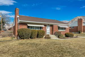 View of front of home featuring brick siding, a front lawn, a chimney, a mountain view, and a shingled roof
