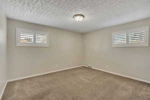 Carpeted spare room featuring a textured ceiling and baseboards