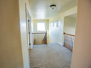Corridor featuring carpet, a textured ceiling, and an upstairs landing