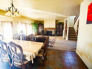 Dining space featuring dark carpet, suspended lighting, and a stone fireplace