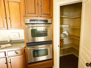 Kitchen featuring stainless steel double oven, wood finish cabinets, dark tile patterned flooring, and light countertops