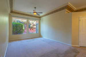 Carpeted empty room featuring a ceiling fan and crown molding