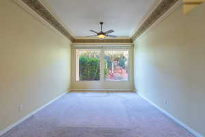 Carpeted spare room featuring ceiling fan and crown molding