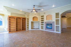 Unfurnished living room featuring a ceiling fan, built in shelves, arched walkways, tile patterned floors, and a tiled fireplace