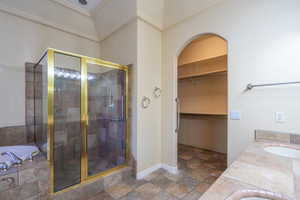Bathroom with double vanity, a stall shower, a bath, a spacious closet, and stone finish flooring