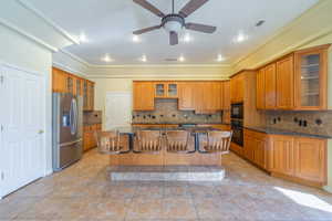 Kitchen featuring glass insert cabinets, a kitchen breakfast bar, a kitchen island with sink, black appliances, and dark stone countertops