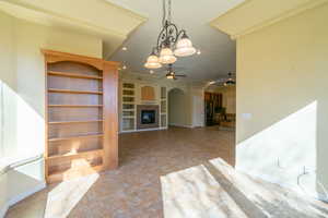 Unfurnished living room with a ceiling fan, a glass covered fireplace, built in shelves, light tile patterned floors, and hanging lights