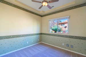 Empty room with wallpapered walls, a tray ceiling, ceiling fan, wainscoting, and carpet