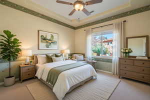 Bedroom featuring wallpapered walls, a raised ceiling, light colored carpet, and a ceiling fan