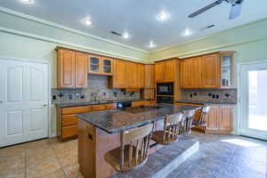 Kitchen with glass fronted cabinets, wood finish cabinets, a breakfast bar area, dark stone countertops, and recessed lighting
