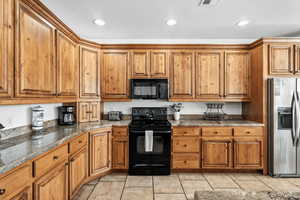 Kitchen featuring wood finish cabinets, black appliances, dark stone counters, light tile patterned floors, and recessed lighting