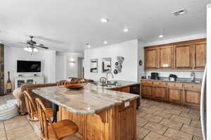 Kitchen featuring wood finish cabinetry, open floor plan, an island with sink, a kitchen breakfast bar, and light stone counters