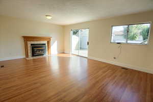 Unfurnished living room with light wood-style flooring, a textured ceiling, and a tiled fireplace