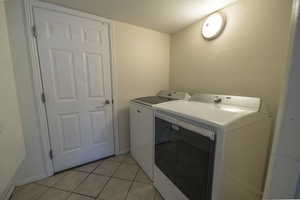 Laundry area featuring a textured ceiling, separate washer and dryer, and light tile patterned flooring