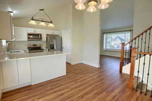 Kitchen with stainless steel appliances, vaulted ceiling, white cabinetry, light wood-style flooring, and hanging lights