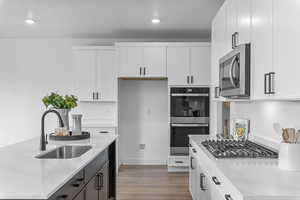 Dual tone kitchen with light stone counters, stainless steel appliances, dark wood-style floors, two tone color scheme, and a kitchen island with sink